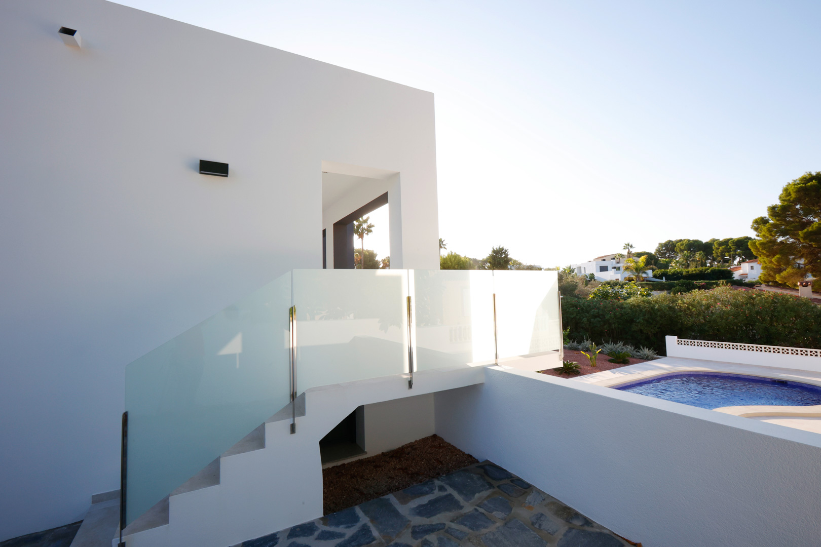 Escalier extérieur avec garde-corps en acier et verre reliant l'espace piscine à l'entrée supérieure de la villa blanche.