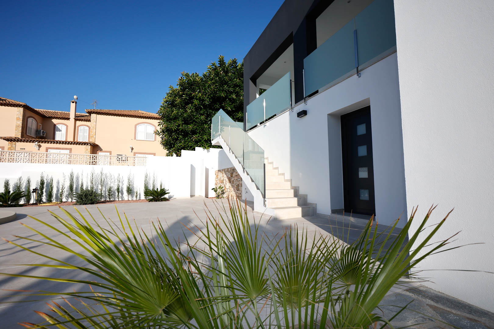 Façade moderne avec escalier extérieur, garde-corps en verre et acier, terrasse en grès cérame et accès indépendant au rez-de-chaussée.