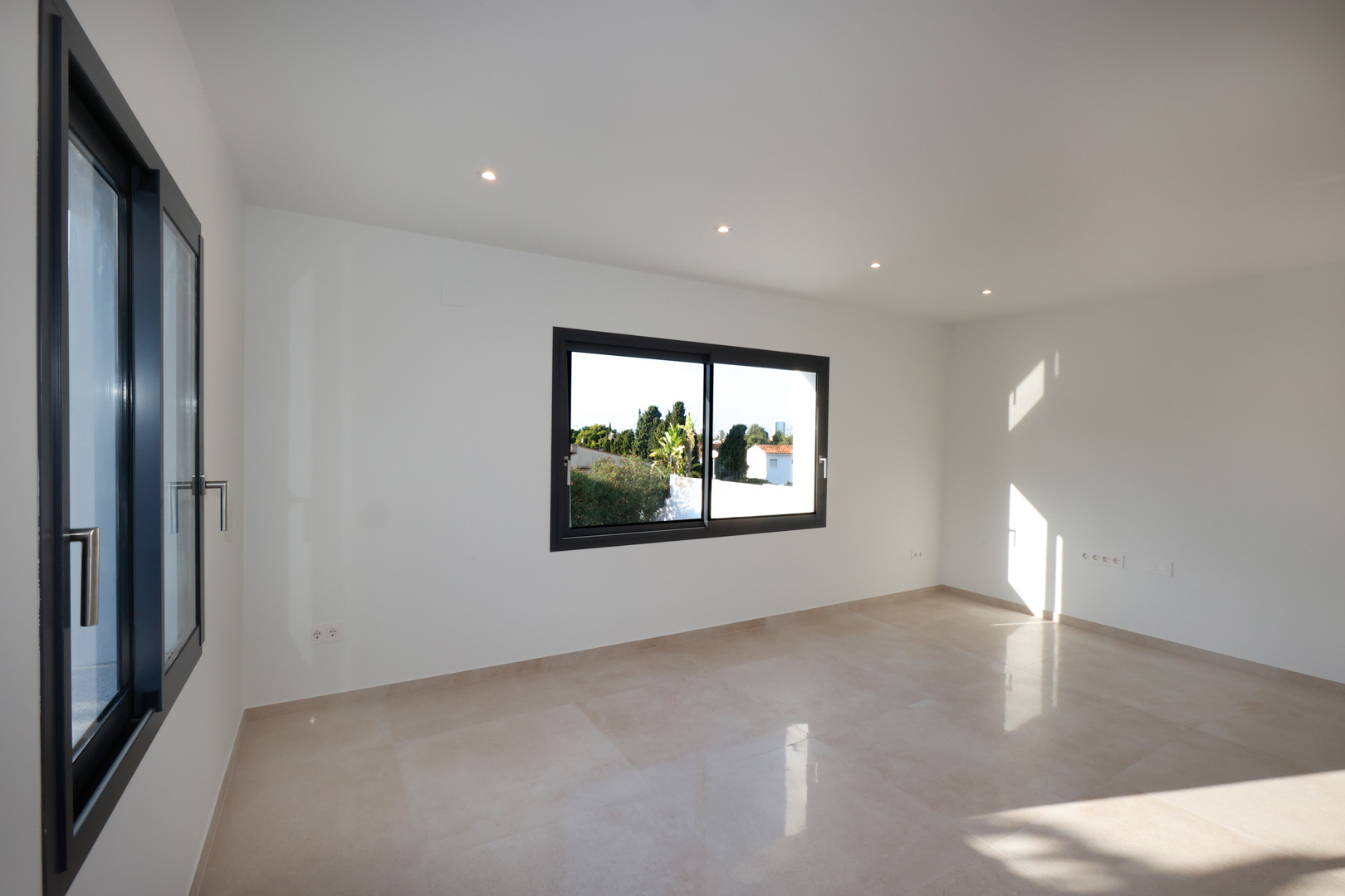 Pièce lumineuse avec sol en grès cérame, menuiserie Technal en gris anthracite et éclairage LED encastré au plafond.