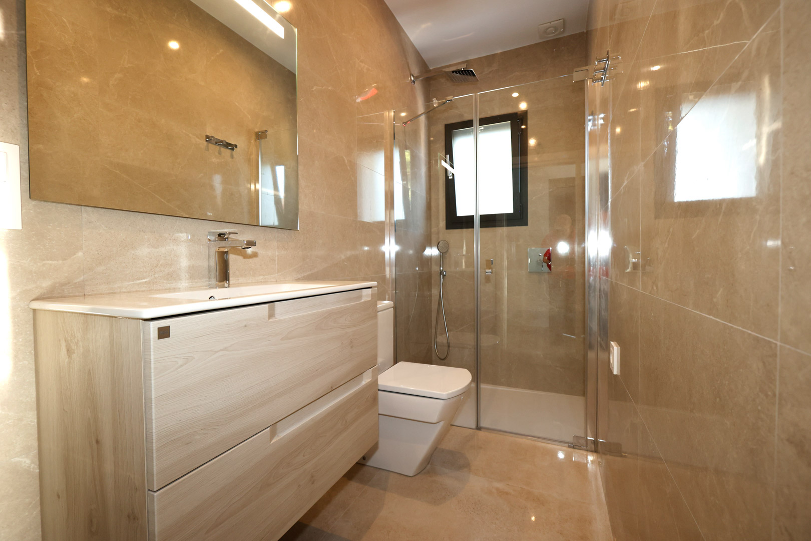 Salle de bain moderne avec meuble sous-vasque en bois clair, murs en grès cérame effet marbre et douche vitrée avec robinetterie chromée.