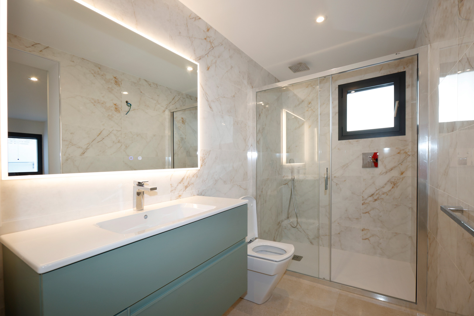 Salle de bain moderne avec meuble vasque vert sauge, miroir rétroéclairé par LED et douche à l'italienne avec parois en verre et carrelage effet marbre.