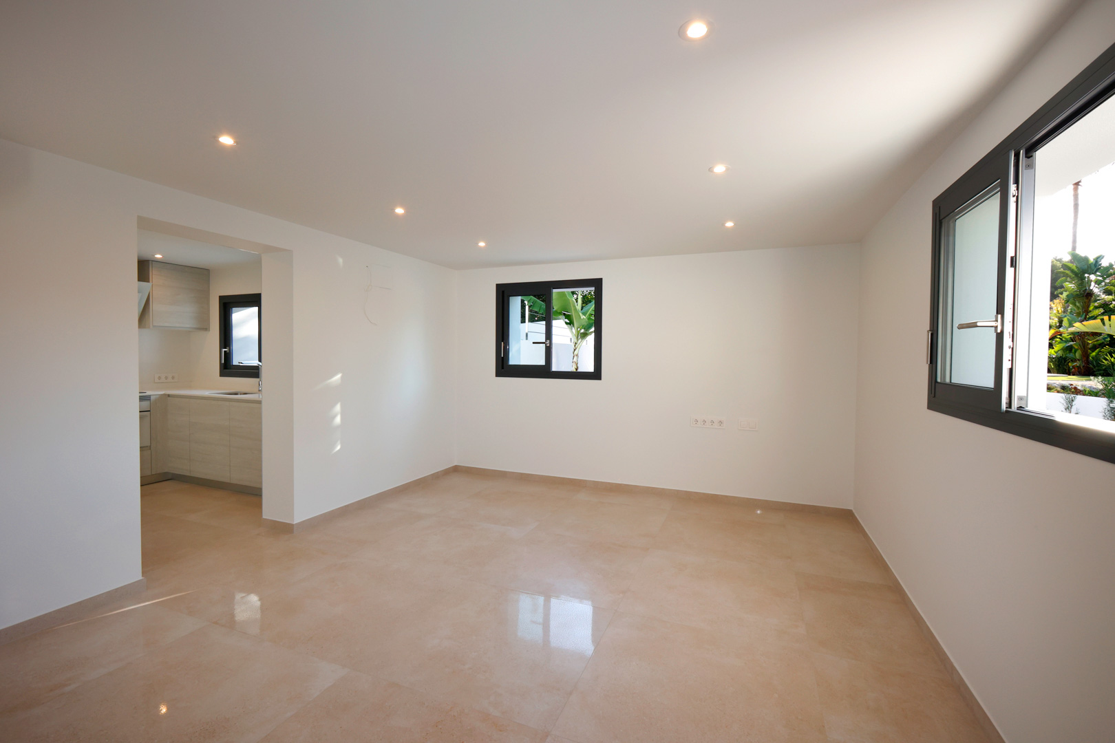 Salon-salle à manger lumineux avec sol en grès cérame, éclairage LED intégré et fenêtres Technal offrant une vue sur la végétation extérieure.
