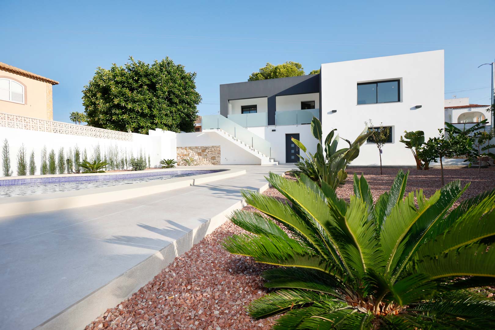 Villa moderne à deux niveaux avec piscine, jardin en gravier rouge et escalier extérieur avec garde-corps en verre reliant les appartements.