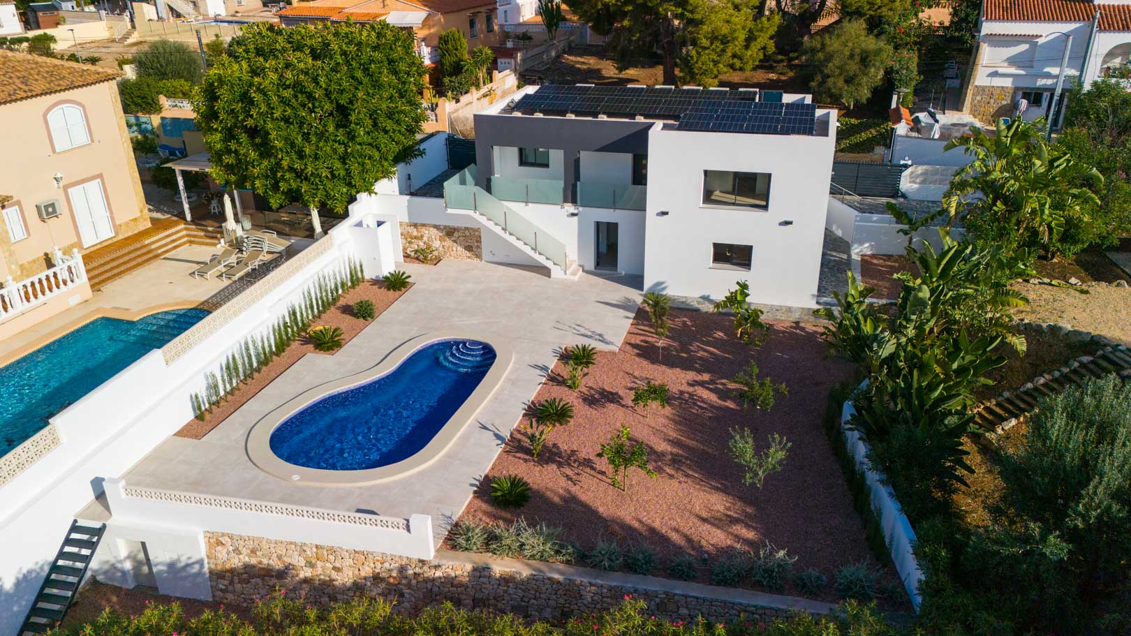 Vue aérienne de la villa avec piscine haricot, jardin en gravier rouge et panneaux solaires. Notez les garde-corps en verre et les murs en pierre naturelle.