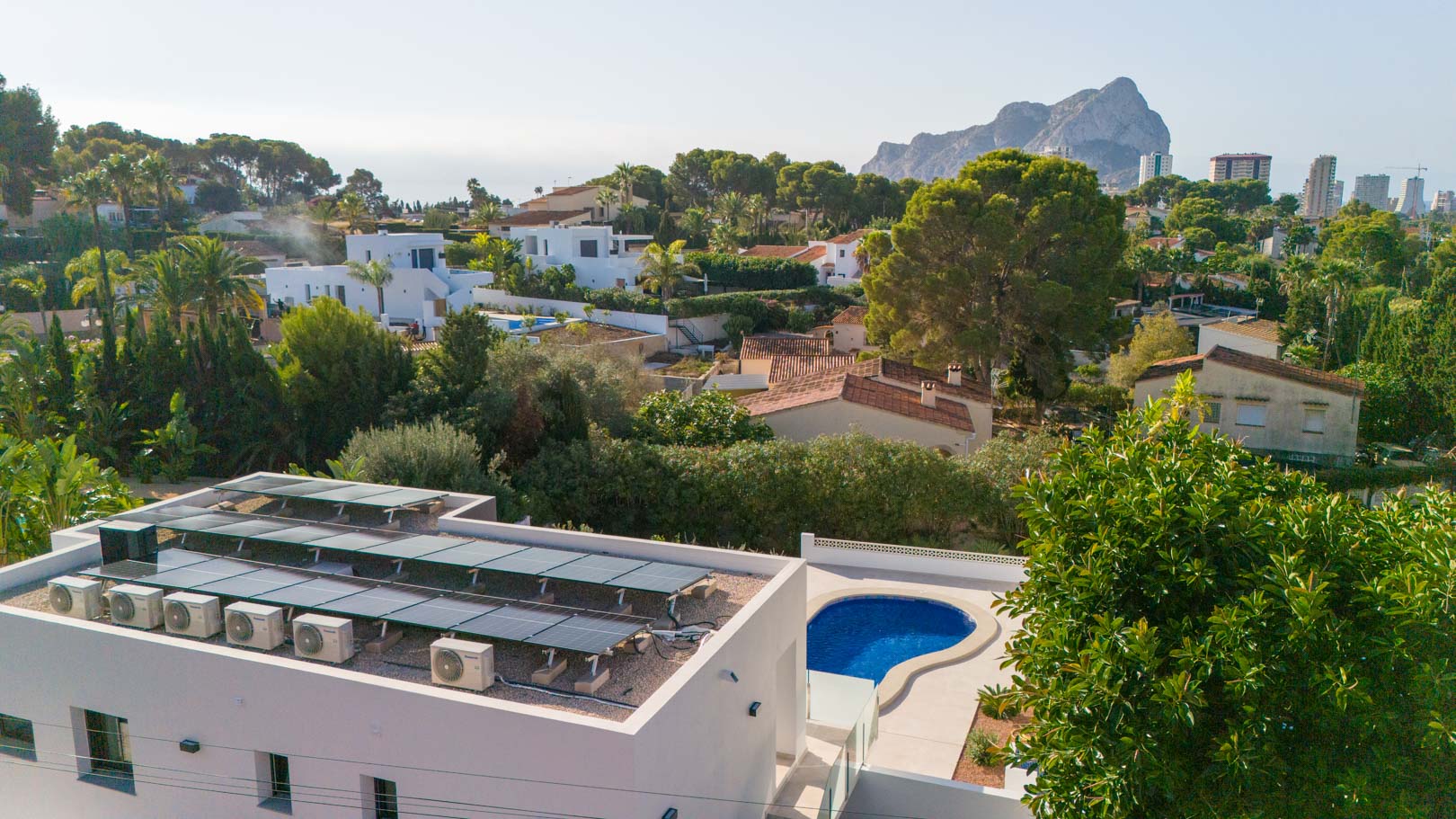 Vue aérienne présentant l'installation solaire photovoltaïque en toiture, la piscine privée et la vue imprenable sur le Peñón de Ifach.