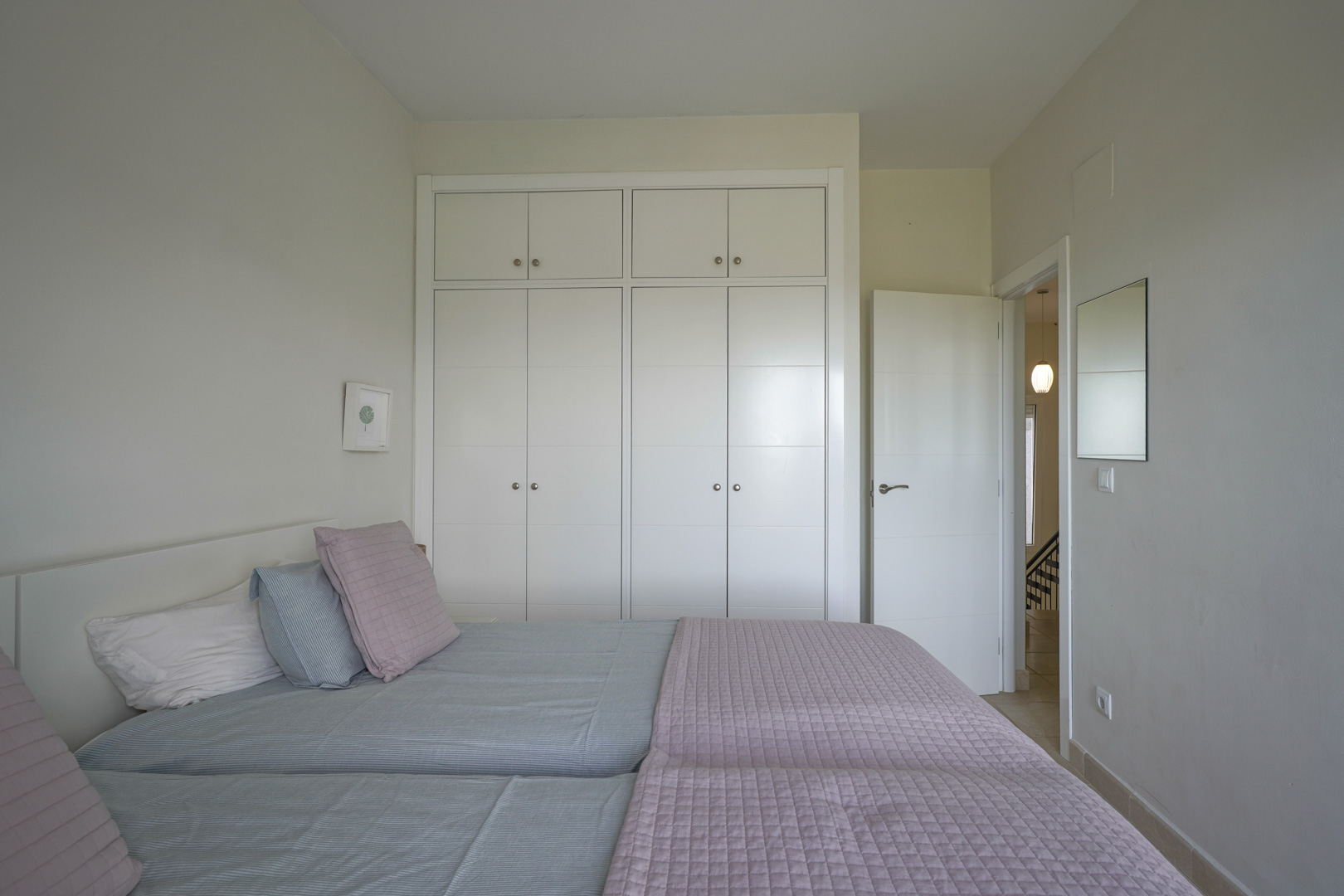 Chambre lumineuse avec de grands placards encastrés blancs et un sol en céramique. Le design épuré offre une atmosphère sereine et fonctionnelle.