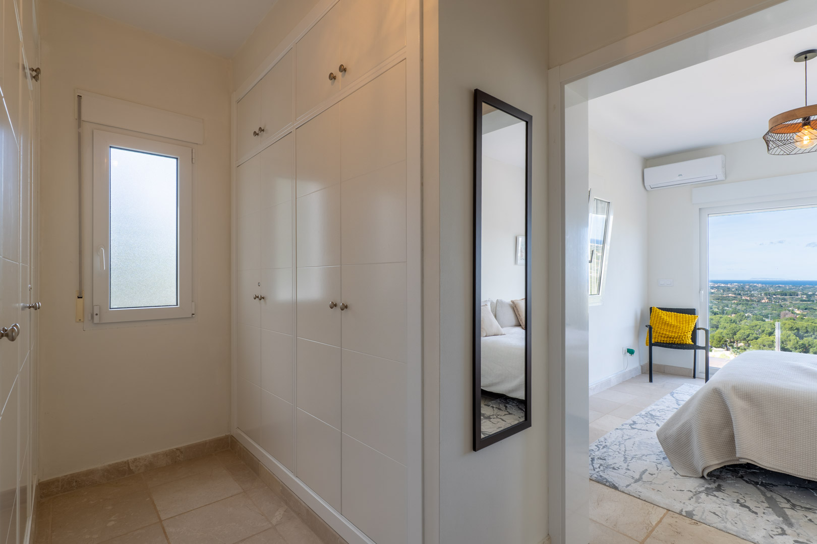 Couloir avec placards intégrés blancs et miroir, menant à une chambre offrant une vue dégagée sur la mer et équipée de la climatisation.