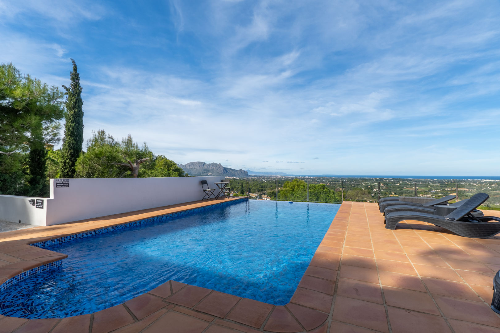Piscine avec mosaïque bleue et terrasse en terre cuite, offrant une vue panoramique sur la mer Méditerranée et le massif du Montgó.