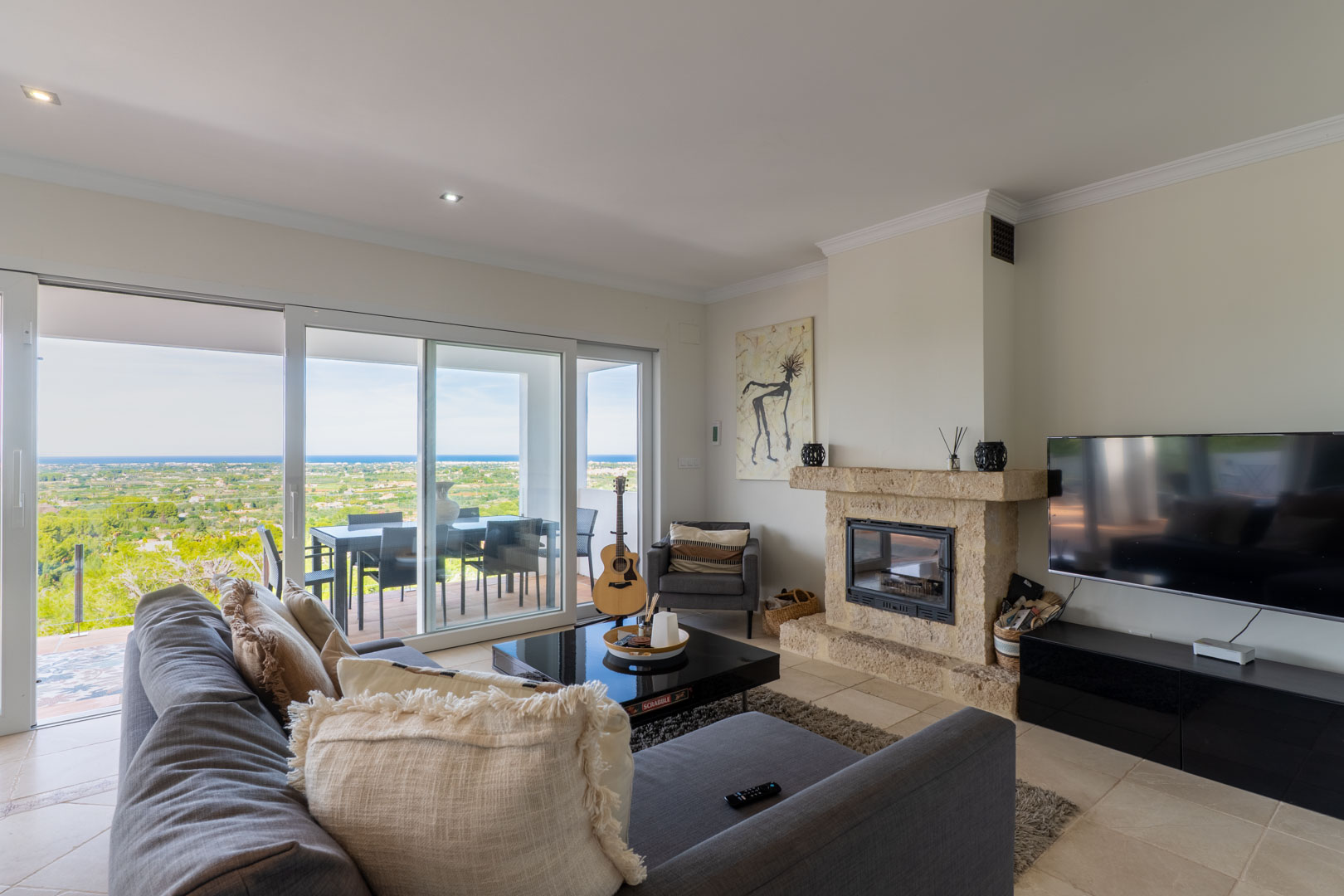 Salon lumineux avec cheminée en pierre naturelle, grandes baies vitrées coulissantes ouvrant sur la terrasse et vues panoramiques sur la mer Méditerranée.