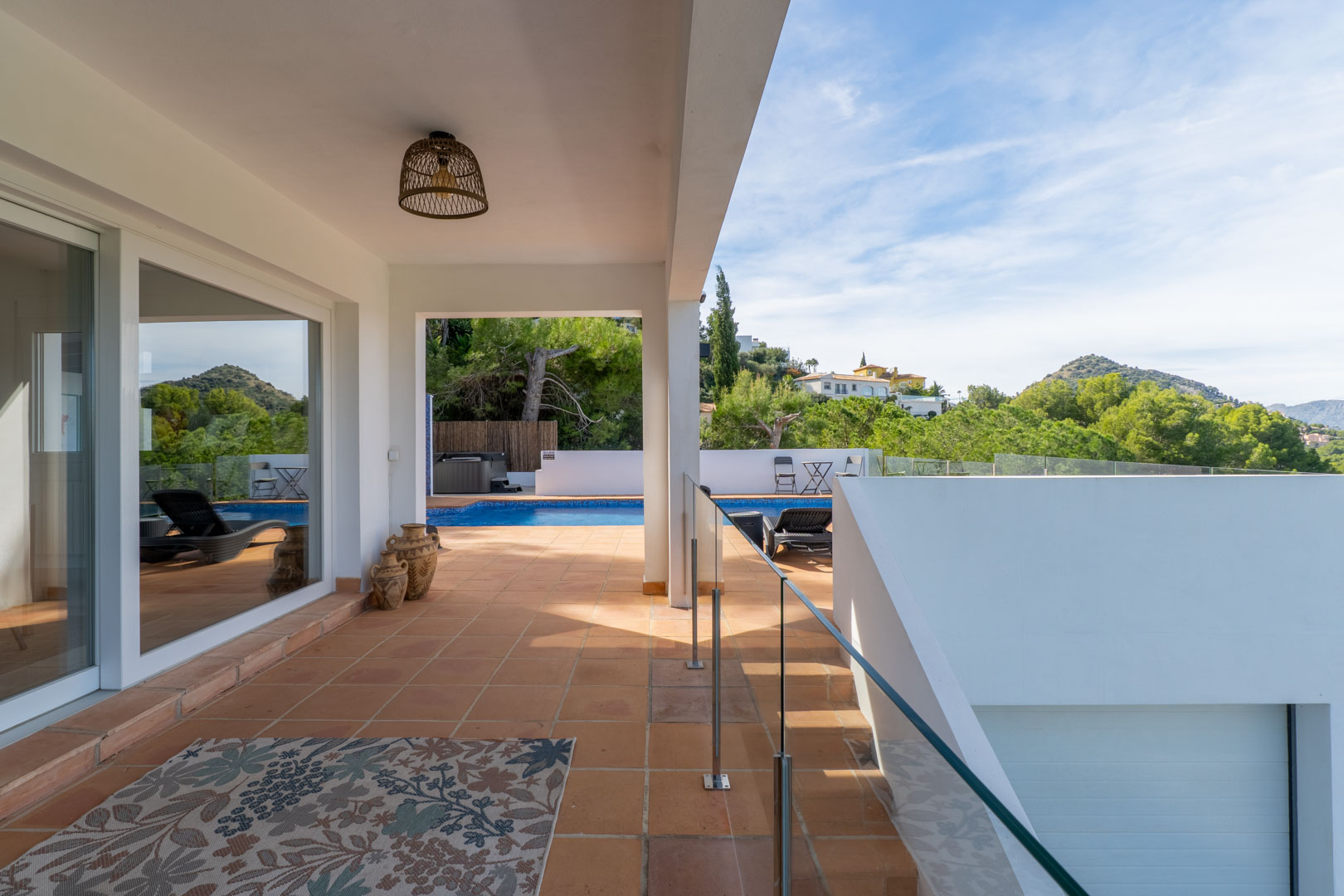 Terrasse couverte avec sol en terre cuite, garde-corps en verre et vue sur la piscine. Décorée de jarres traditionnelles et d'une suspension en rotin.