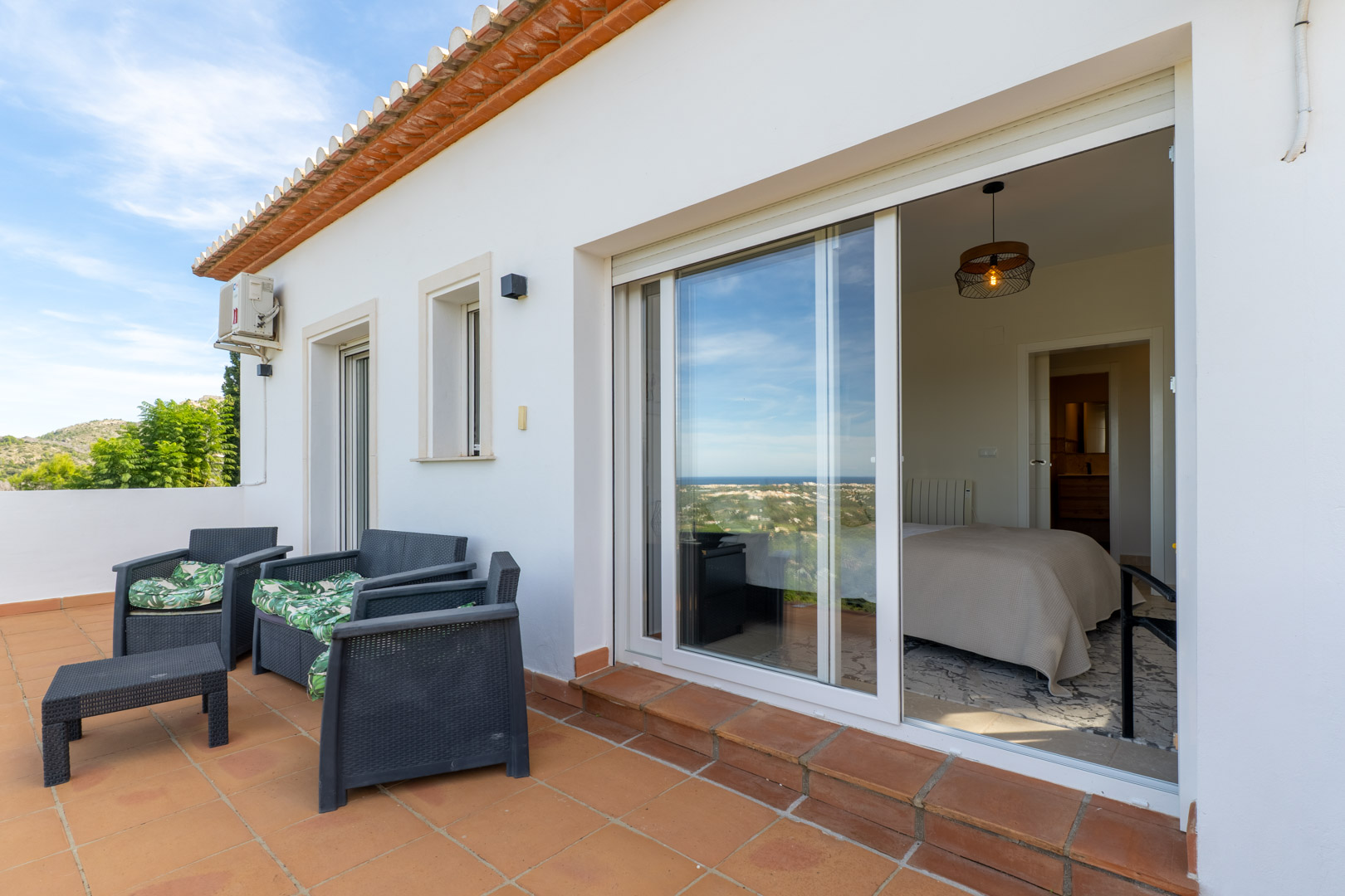 Terrasse supérieure avec carrelage en terre cuite et mobilier de jardin, offrant un accès direct à la chambre et une vue dégagée sur la côte méditerranéenne.