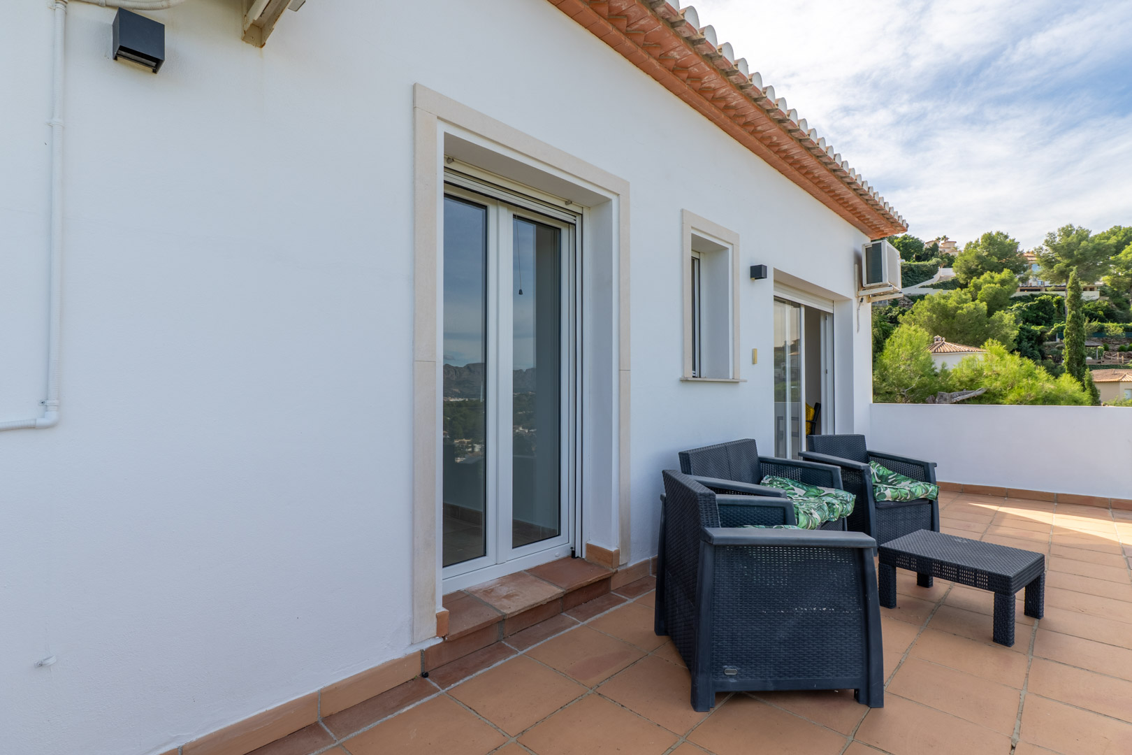 Terrasse supérieure avec sol en terre cuite, mobilier de jardin en résine tressée et accès direct aux chambres par des portes-fenêtres coulissantes.