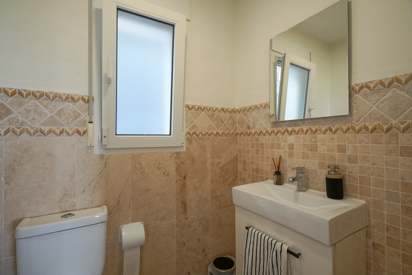 Toilettes invités avec carrelage aux tons naturels, frise décorative, lavabo moderne et fenêtre en verre dépoli pour une luminosité optimale.