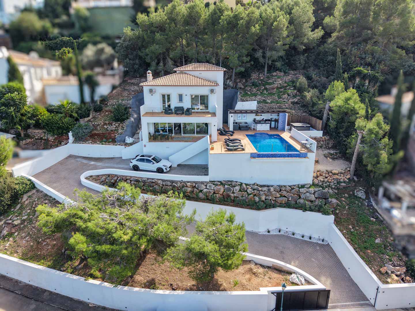 Vue aérienne de la villa méditerranéenne avec piscine à débordement, cuisine d'été et terrasses, nichée sur un terrain arboré de pins à La Sella.