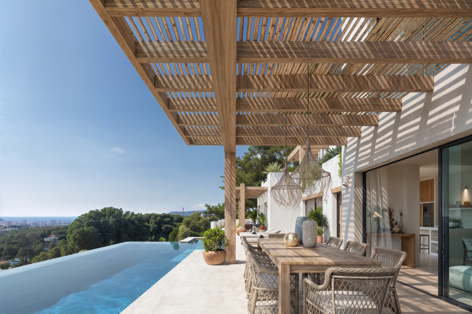 Terrasse extérieure avec pergola en bois, espace dînatoire et piscine à débordement offrant une vue panoramique sur la mer Méditerranée et la côte.