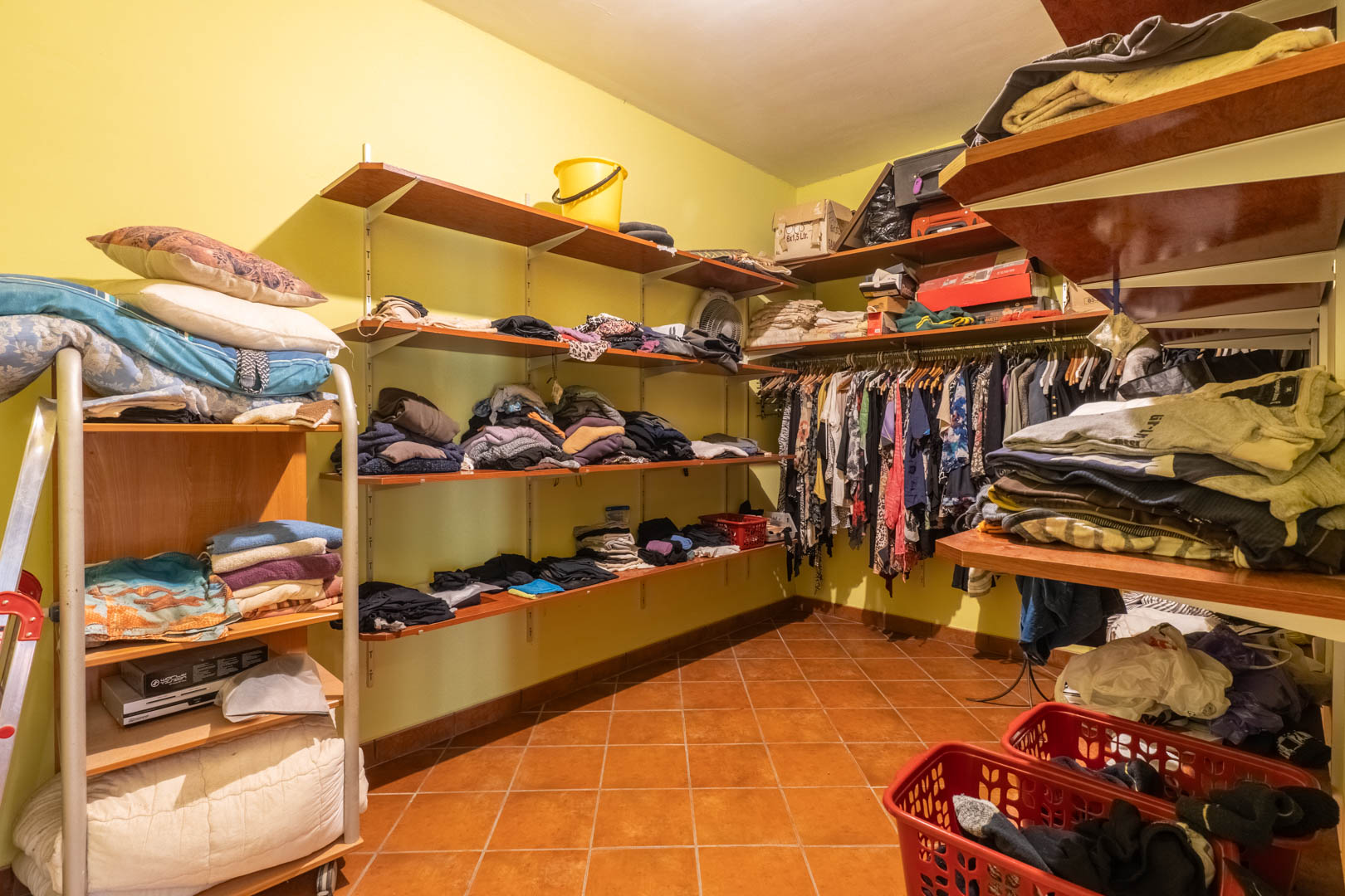 Dressing fonctionnel avec étagères en bois, tringles de rangement et sol en terre cuite rustique, offrant un vaste espace d'organisation et de stockage.