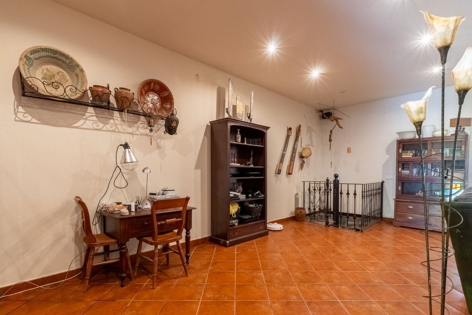 Espace bureau avec pupitre en bois, sol en terre cuite et garde-corps en fer forgé sécurisant l'accès à l'escalier vers le niveau inférieur.