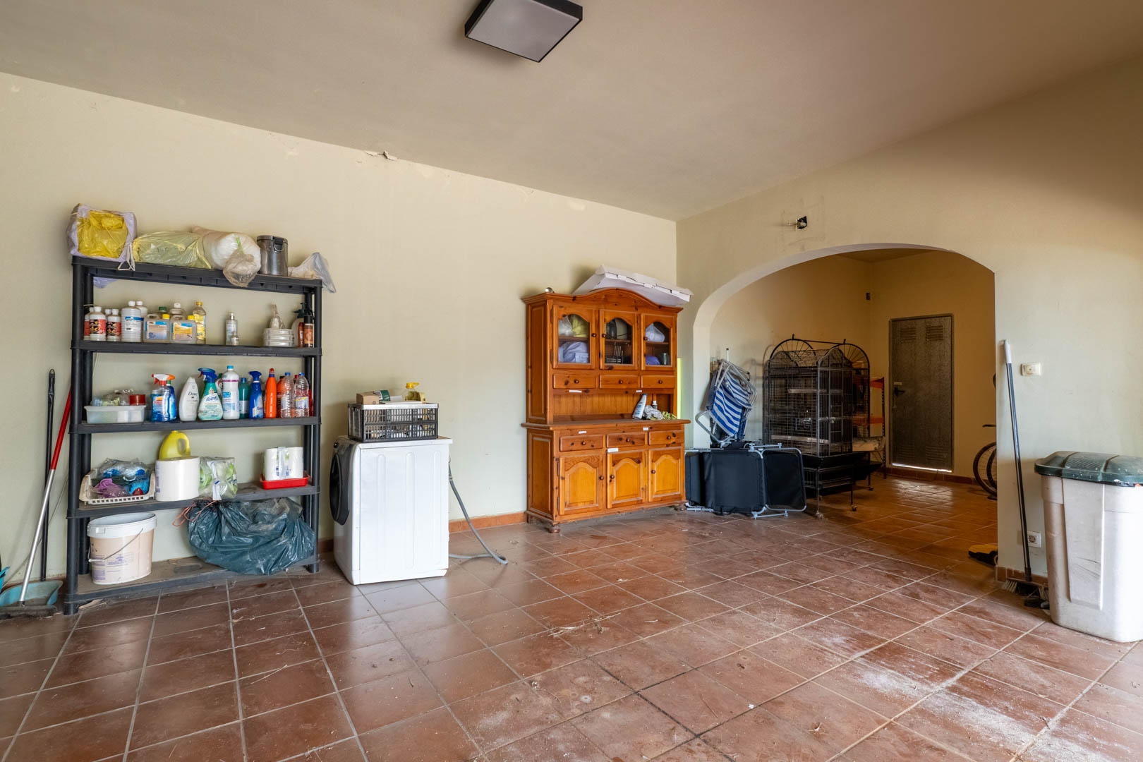 Grand espace de rangement au niveau inférieur avec sol en grès cérame, étagères et arche ouvrant sur la zone de buanderie et le garage.