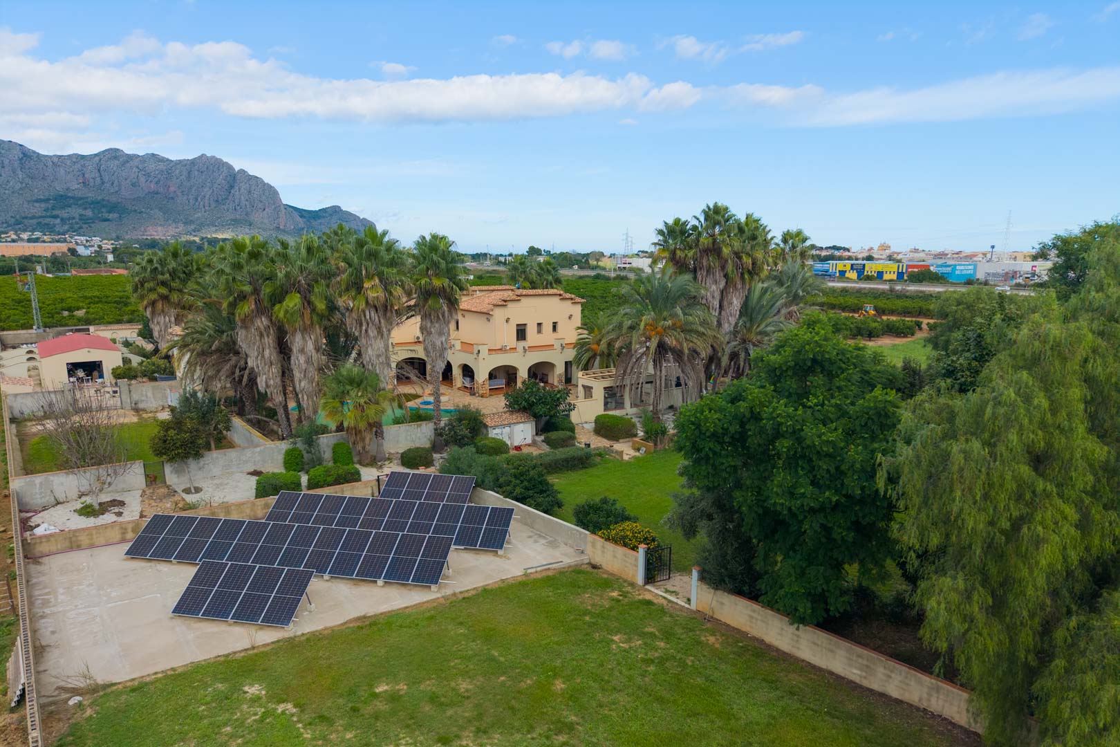 Vue aérienne de la propriété avec son installation photovoltaïque, ses jardins arborés de palmiers et la villa principale au style méditerranéen.