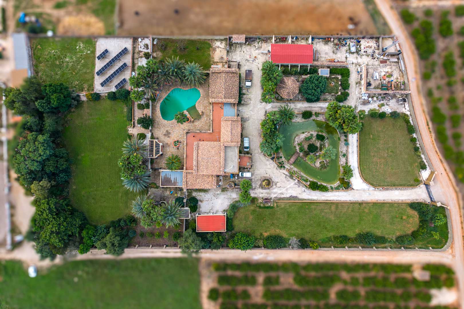Vue aérienne de la propriété montrant la maison principale, la piscine, l'étang japonais, les vastes jardins et l'installation de panneaux solaires sur le terrain.