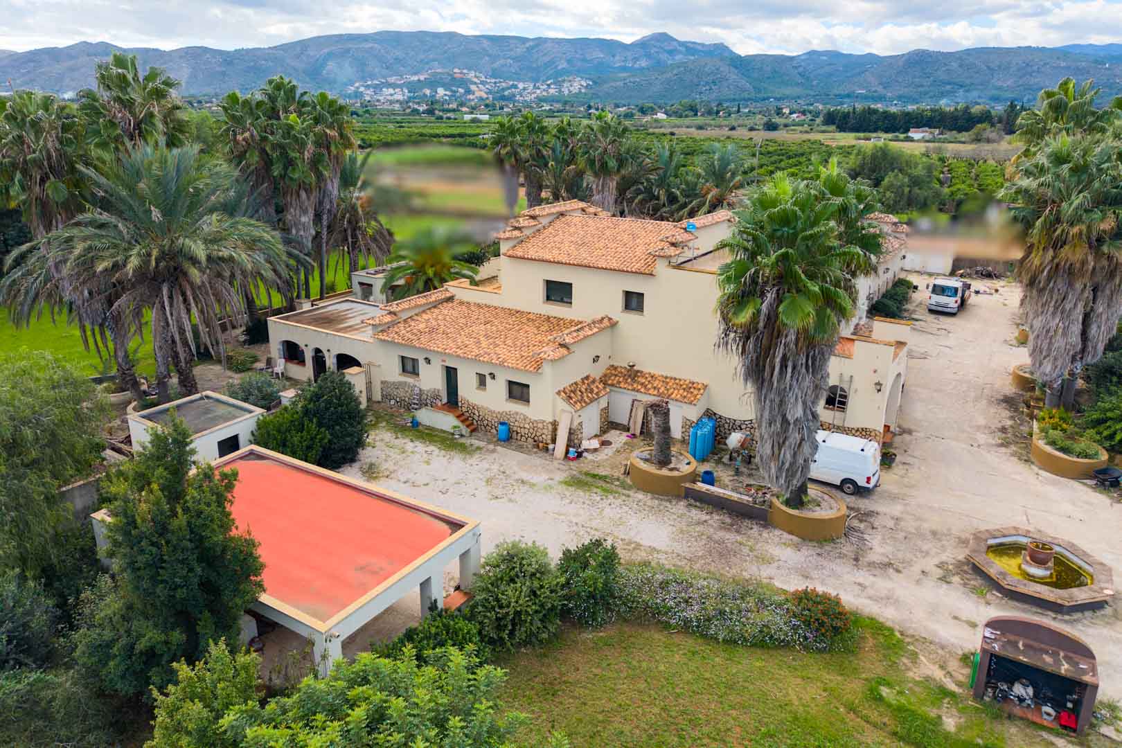 Vue aérienne de la villa méditerranéenne aux toits de terre cuite, entourée de palmiers et de jardins avec un panorama sur la vallée et les montagnes.