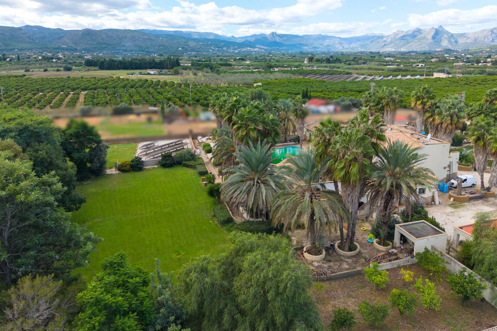 Vue aérienne du vaste domaine avec ses jardins de palmiers, sa pelouse et sa piscine, entouré de vergers et offrant un panorama sur les montagnes.