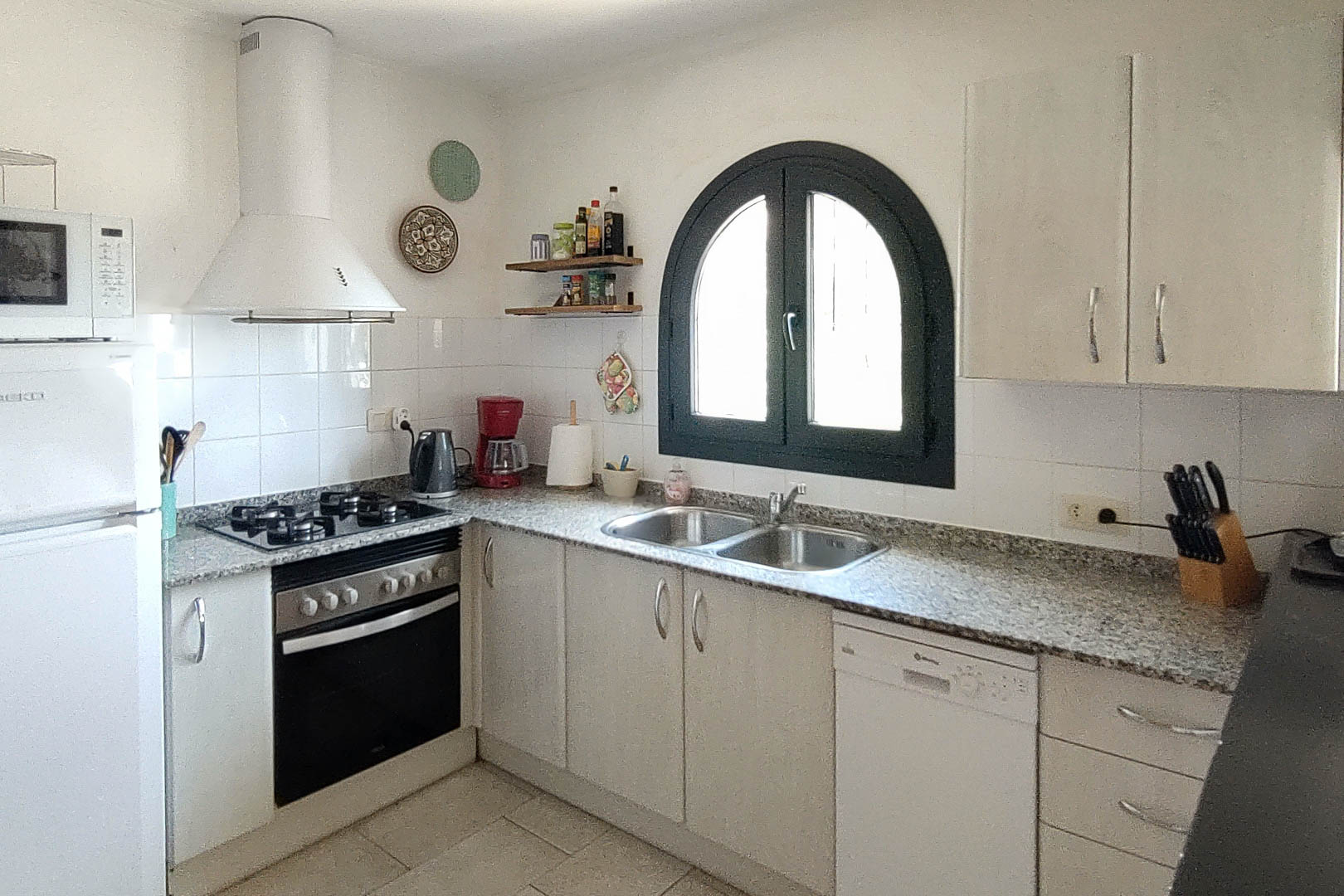 Cuisine fonctionnelle avec plan de travail en granit, équipée d'une plaque de cuisson au gaz. Une fenêtre en arche avec cadre sombre apporte une luminosité naturelle à l'espace.