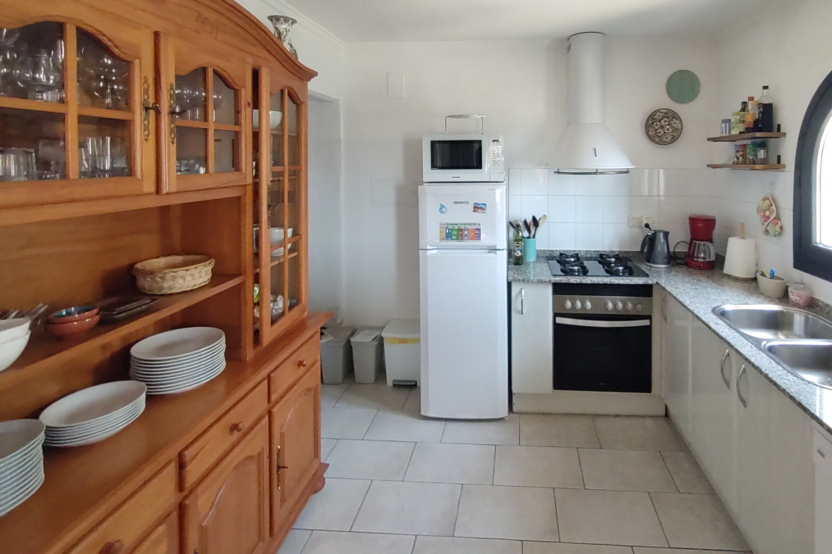 Cuisine fonctionnelle avec plan de travail en granit, plaque de cuisson au gaz et un grand vaisselier en bois massif sur un sol en carrelage clair.