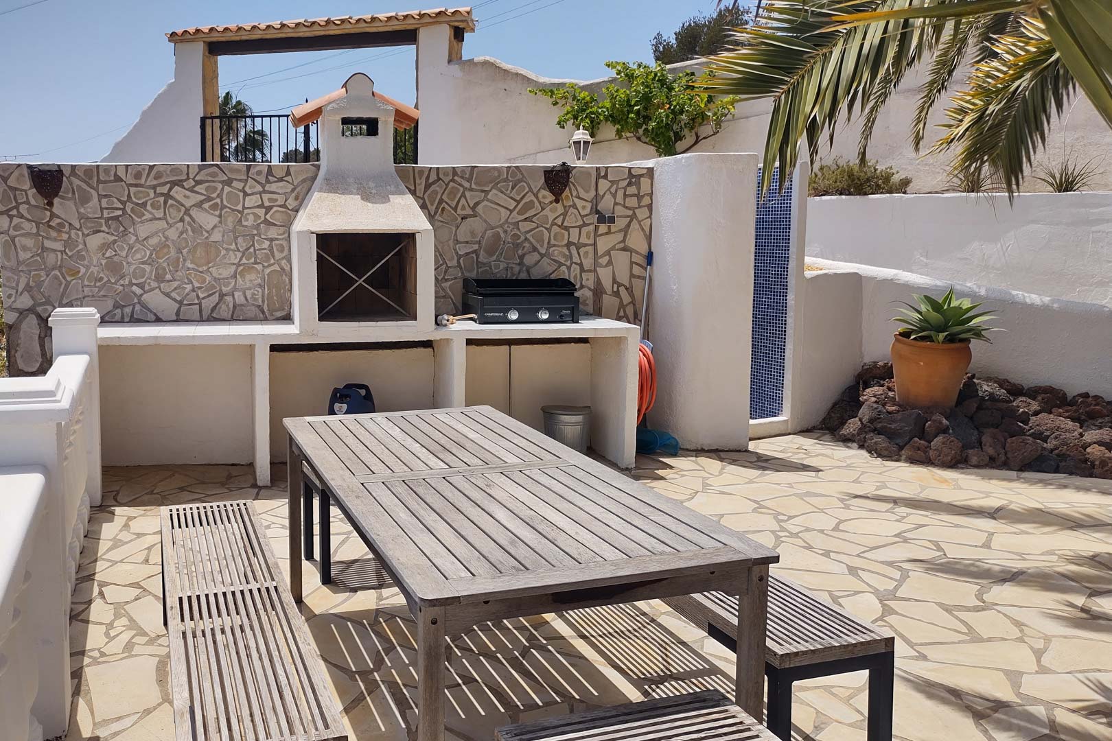 Espace barbecue maçonné avec grill à gaz, table de pique-nique en bois et dallage en pierre naturelle, complété par une douche extérieure carrelée de bleu.
