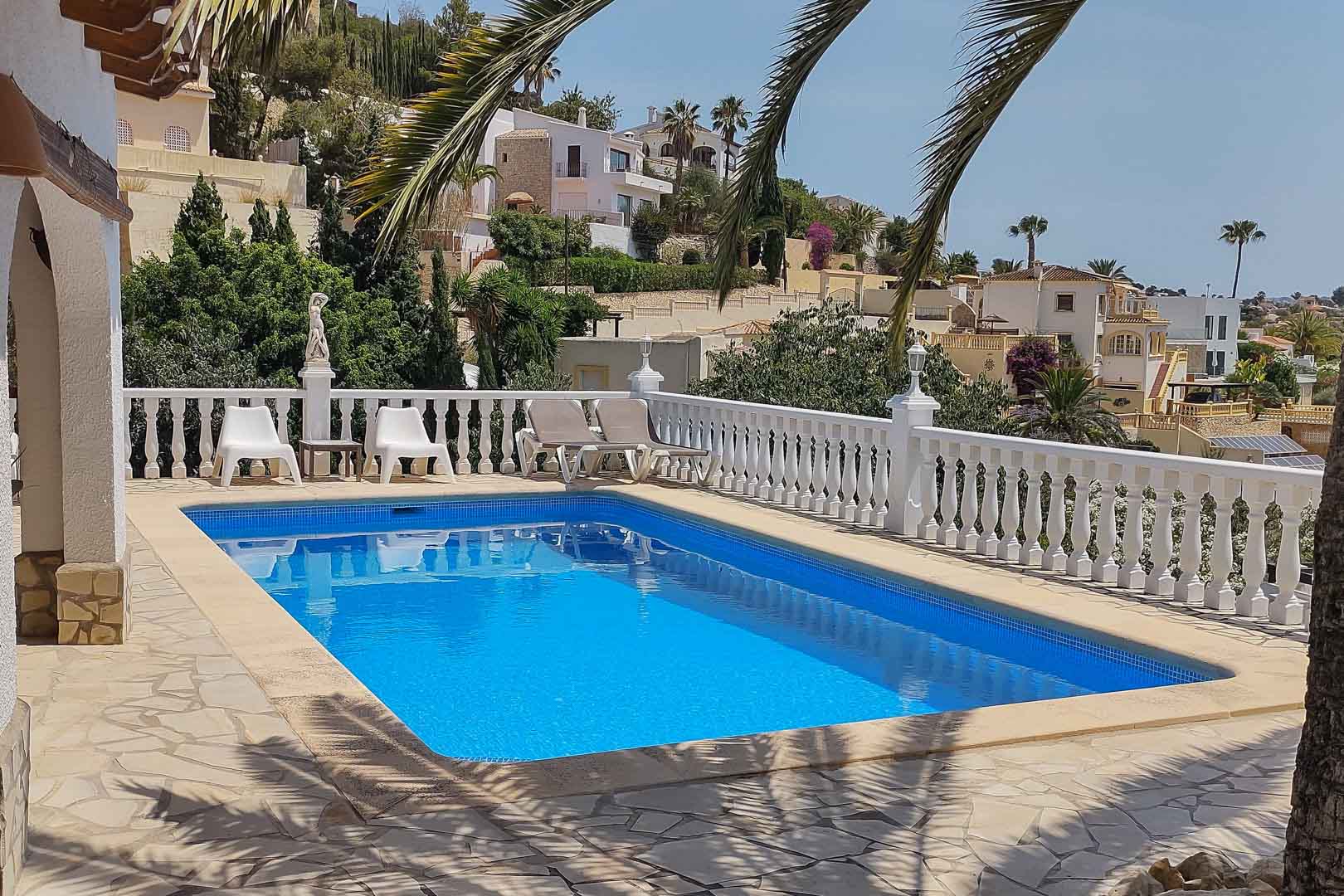 Piscine rectangulaire en mosaïque bleue, entourée d'une terrasse en pierre et d'une balustrade blanche avec vue sur les collines résidentielles environnantes.