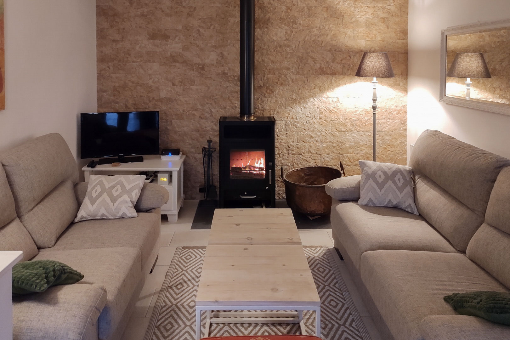 Salon chaleureux avec poêle à bois sur un mur en pierre naturelle, aménagé avec des canapés aux tons neutres et une table basse en bois clair.