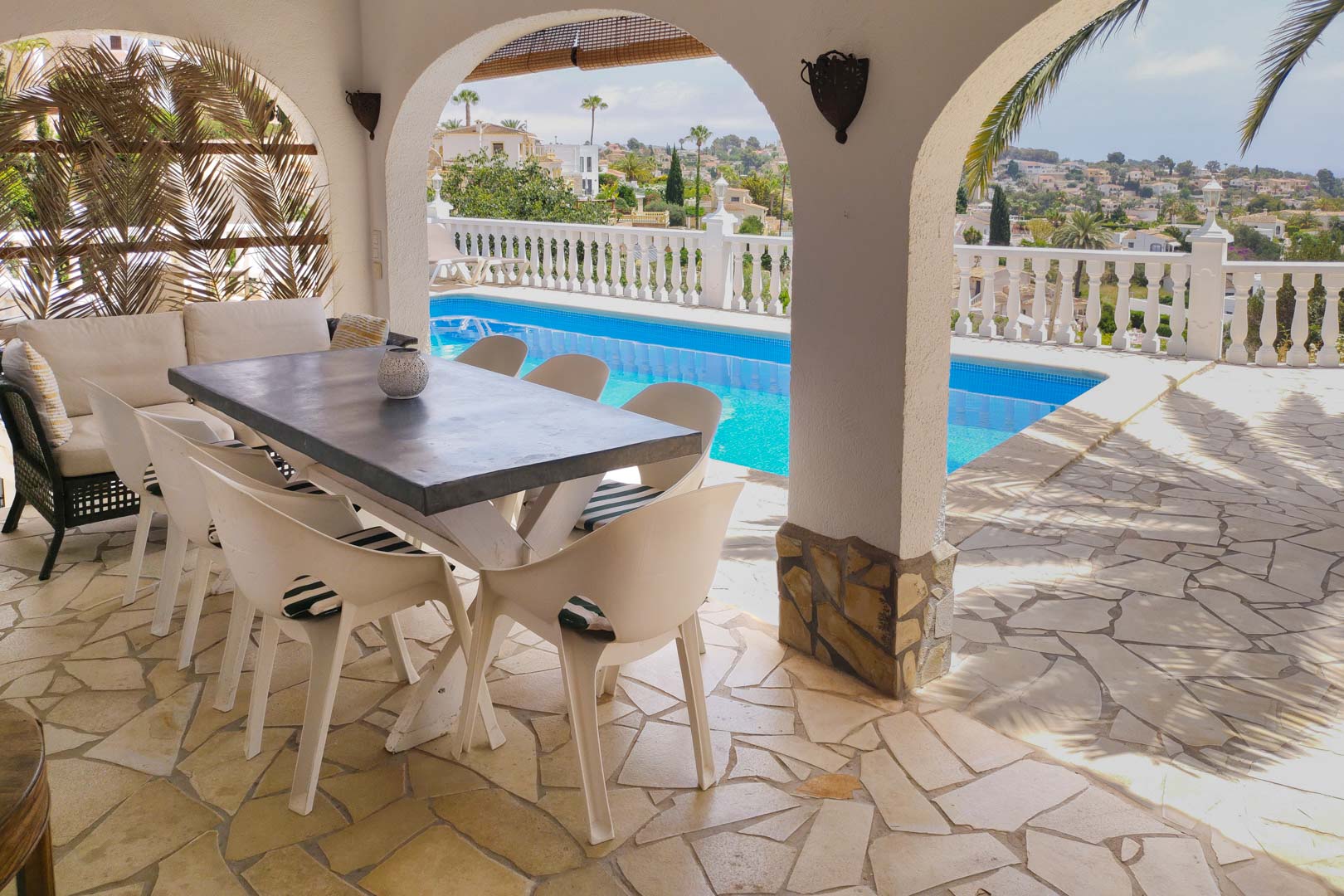 Terrasse couverte avec arches traditionnelles, sol en pierre naturelle et coin repas offrant une vue sur la piscine et la vallée environnante.