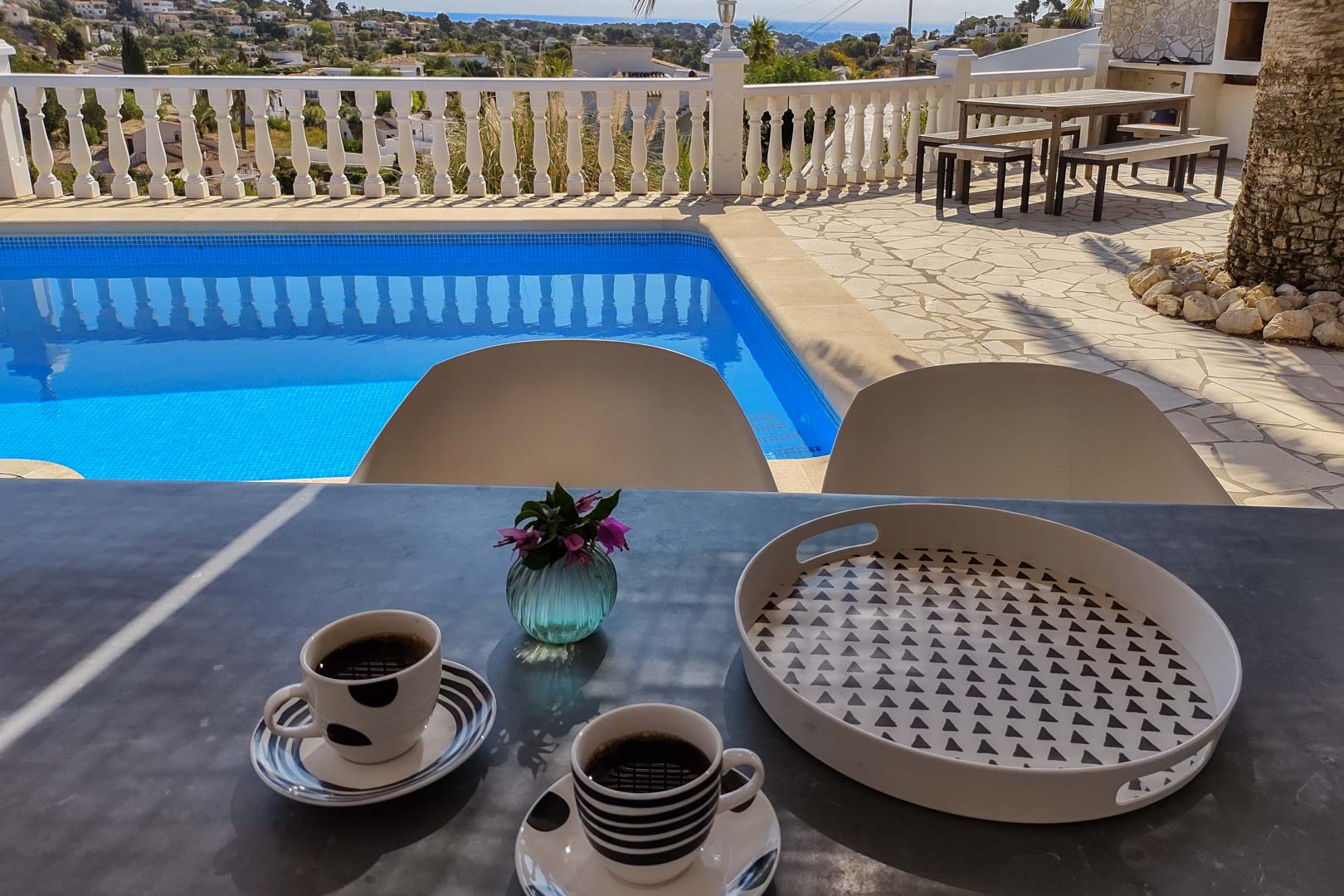 Terrasse principale avec piscine privée et vue sur mer. Comprend un coin repas extérieur avec table et bancs en bois sur un sol en pierre naturelle et balustrade blanche.