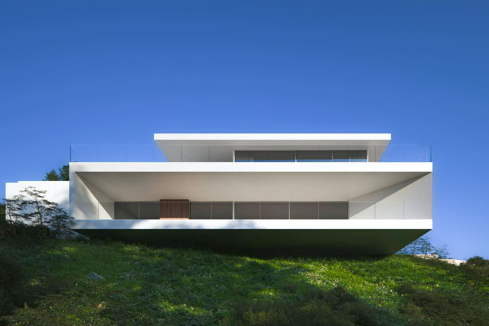 Façade avant-gardiste aux lignes blanches épurées et volumes en porte-à-faux, avec de vastes terrasses vitrées intégrées dans la colline de Moraira.