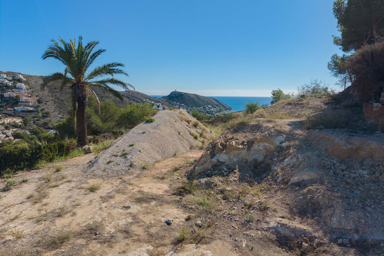Terrain à bâtir en préparation offrant une vue panoramique sur la mer Méditerranée et la côte de Moraira, entouré de végétation locale et de palmiers.
