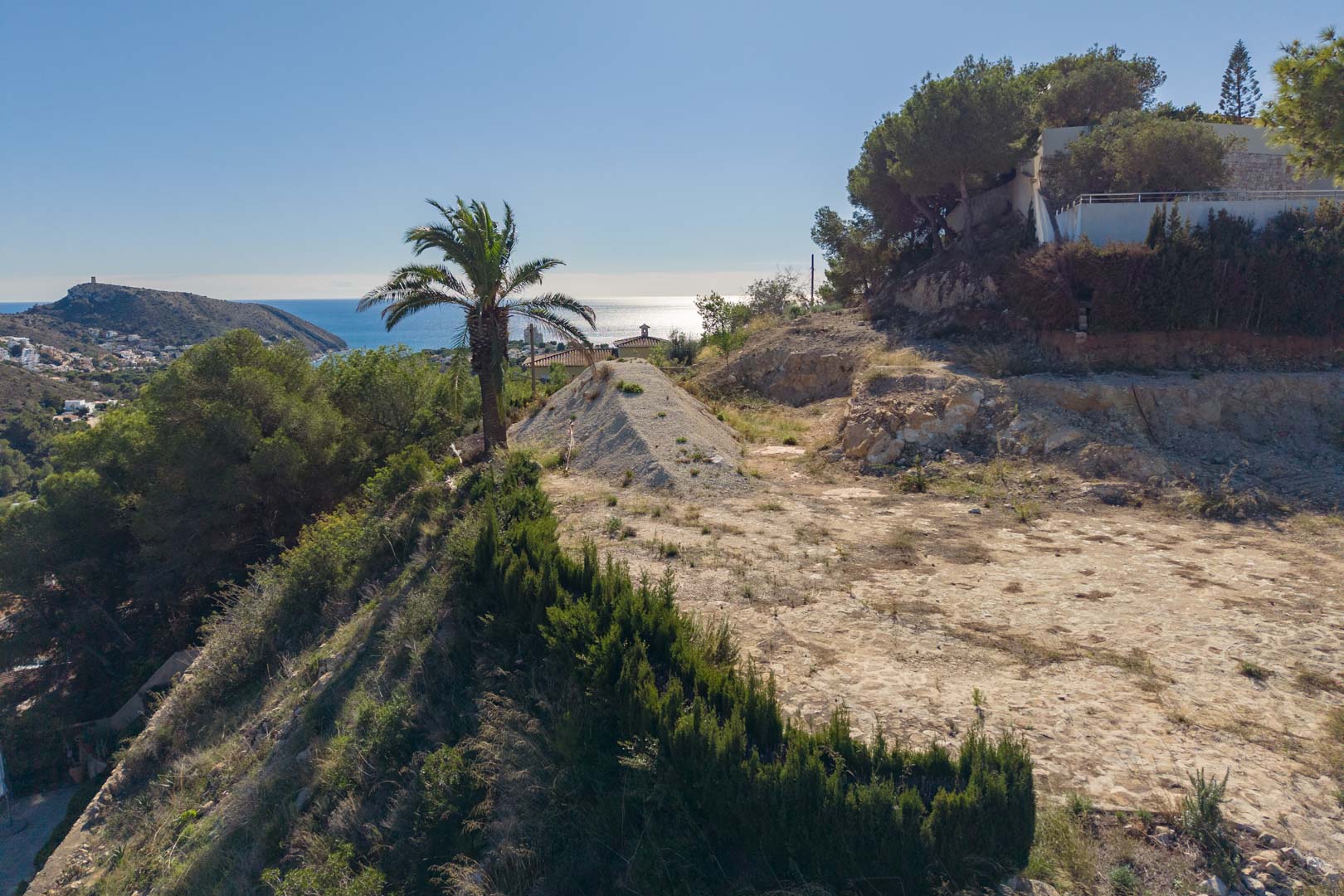 Terrain constructible surélevé à Moraira offrant une vue panoramique sur la mer Méditerranée et El Portet, entouré de pins et d'un environnement naturel préservé.