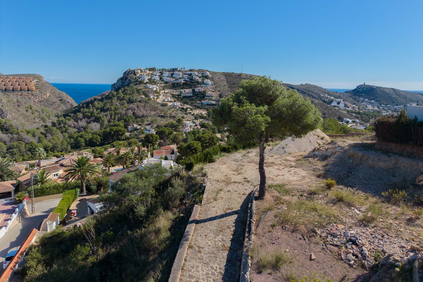 Vues panoramiques surélevées sur la vallée de Moraira et la mer Méditerranée, entourées de pins et d'un paysage côtier préservé.