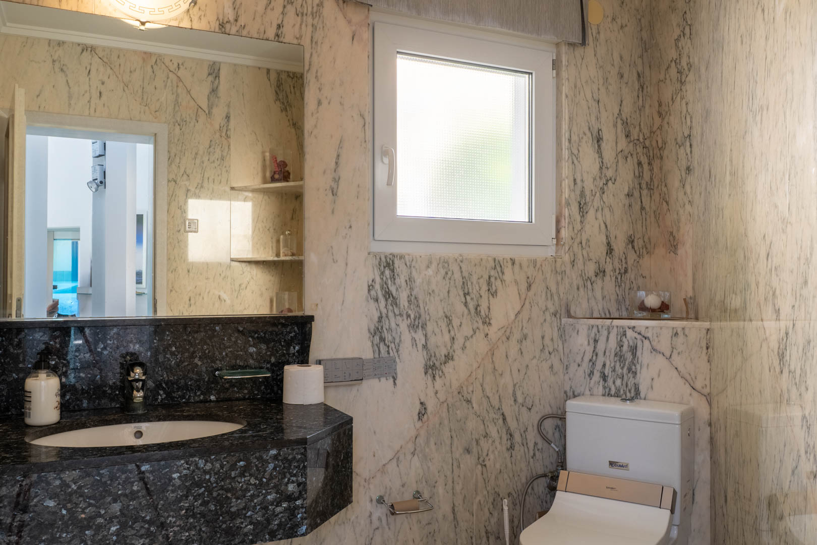 Salle de bain avec murs en marbre veiné et comptoir en granit noir.