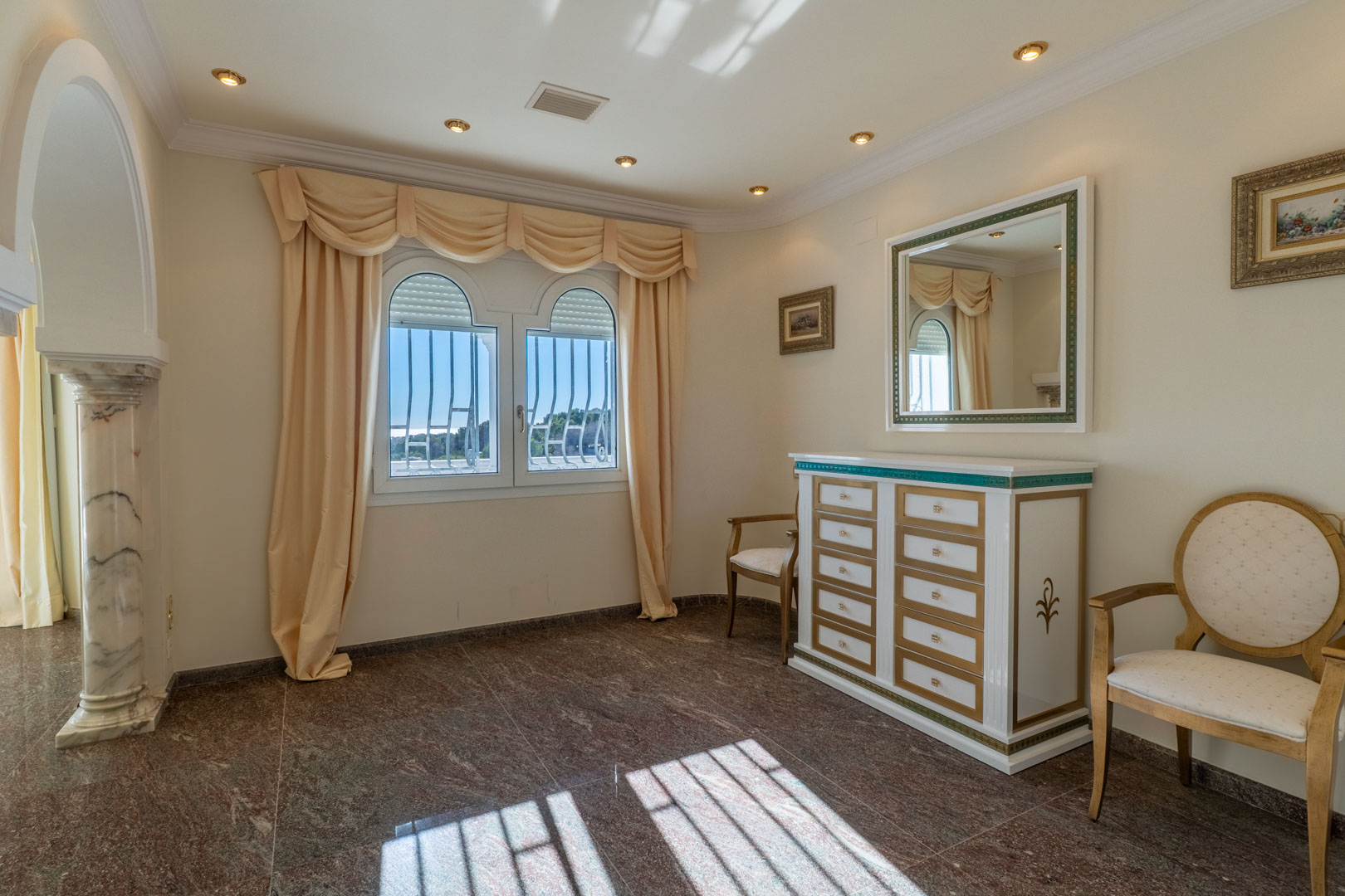 Pièce élégante avec sol en granit poli, commode de style classique et colonne en marbre encadrant une fenêtre cintrée baignée de lumière.