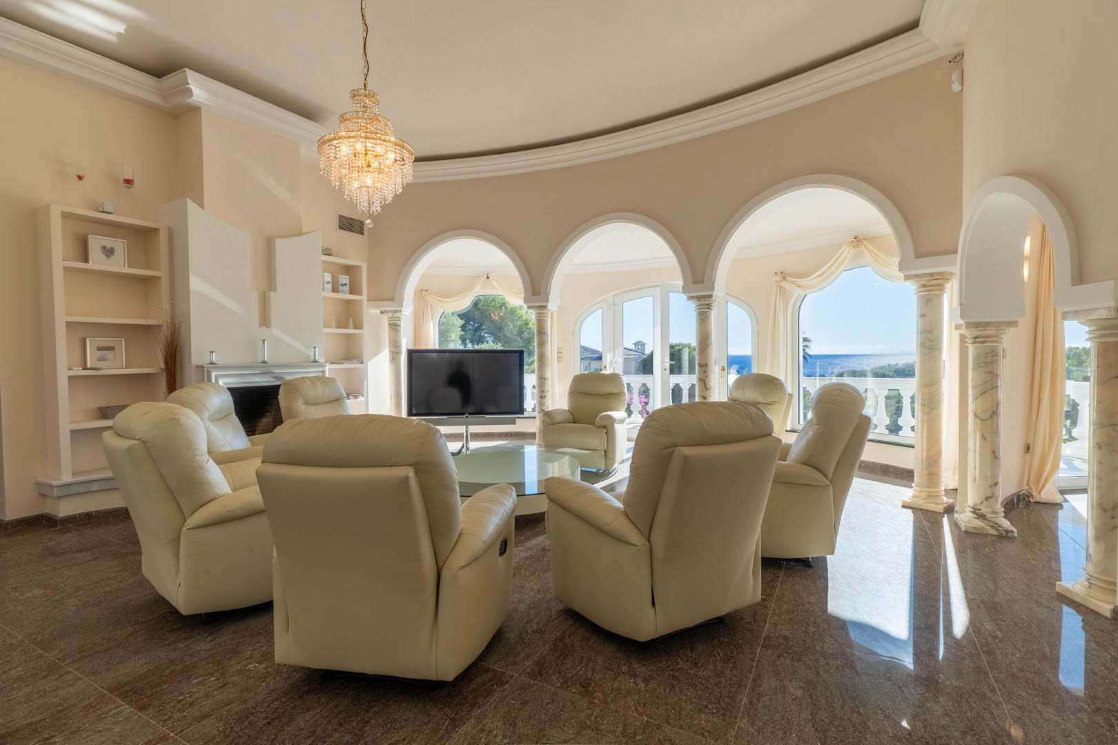 Salon circulaire avec des arches sur colonnes en marbre, fauteuils en cuir crème et vue panoramique sur la mer Méditerranée à travers de grandes baies.