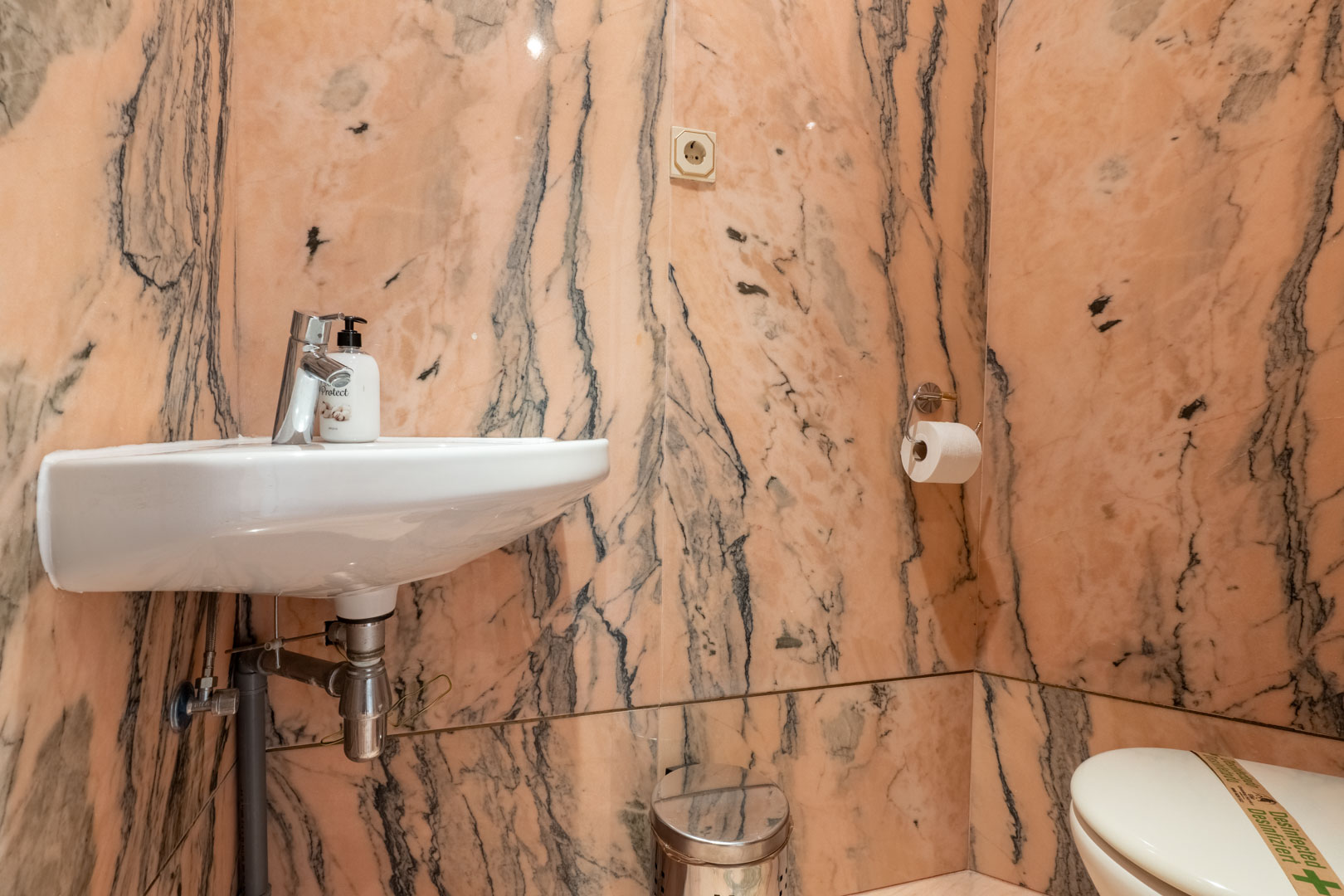 Toilettes invités revêtues de marbre rose aux veines sombres, comprenant un lavabo suspendu blanc et des accessoires en chrome.