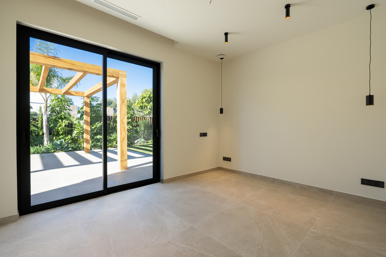 Intérieur minimaliste avec sol en céramique et grandes baies vitrées menant à une terrasse extérieure dotée d'une pergola en bois et d'un jardin paysager.
