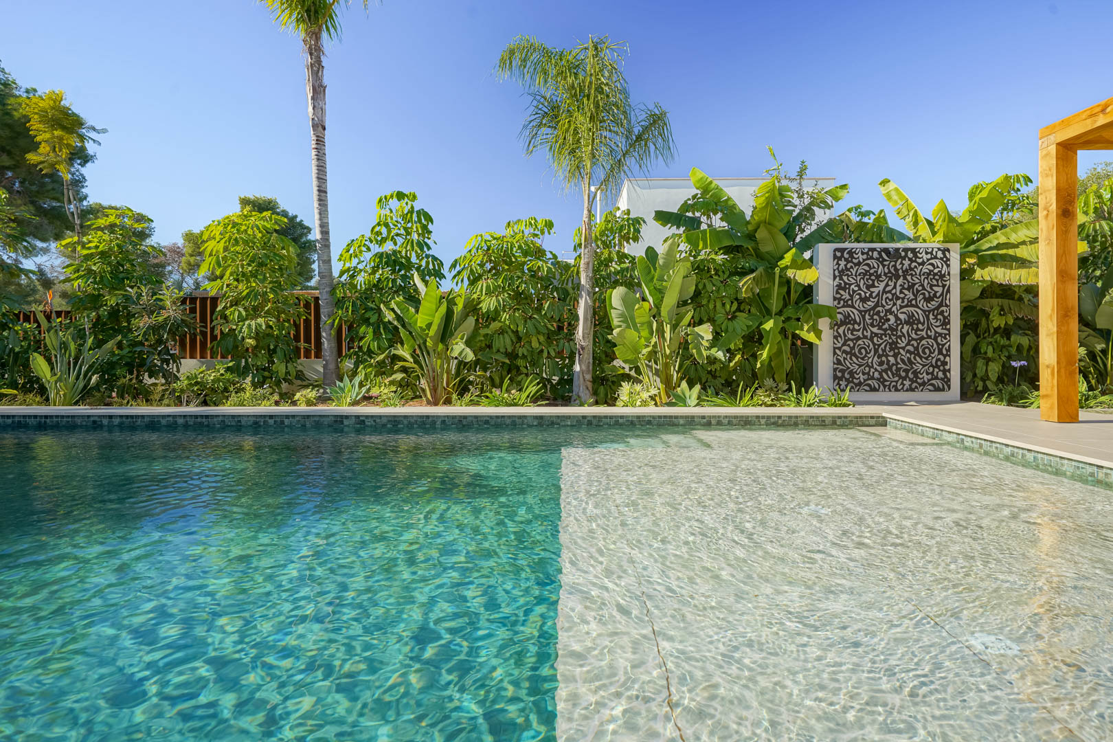 Piscine au sel de style Bali avec plage immergée, entourée d'un jardin méditerranéen luxuriant aux essences tropicales et d'un panneau ornemental.
