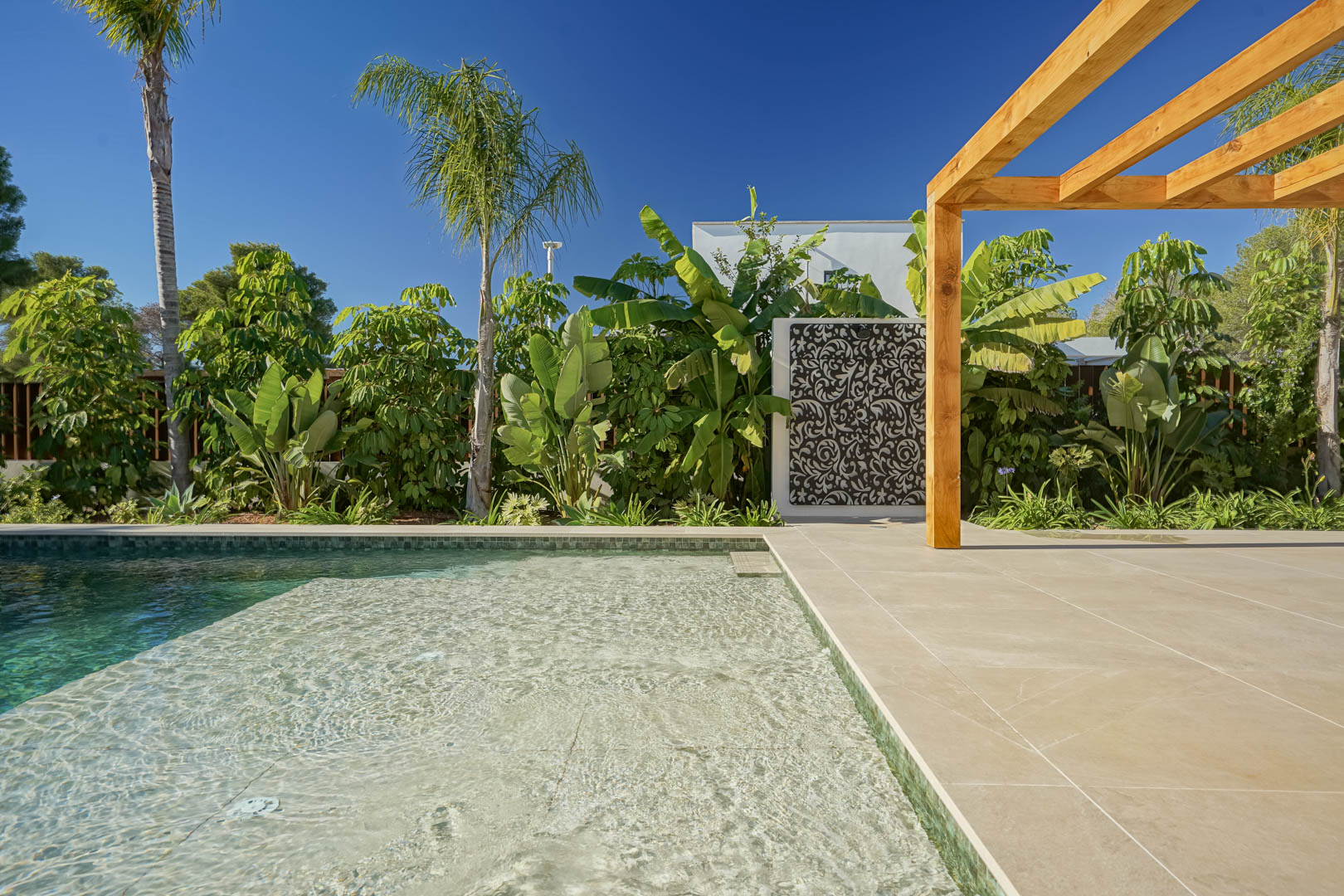 Piscine au sel de style Bali avec plage immergée, terrasse en grès cérame, pergola en bois d'iroko et jardin méditerranéen luxuriant aux accents tropicaux.