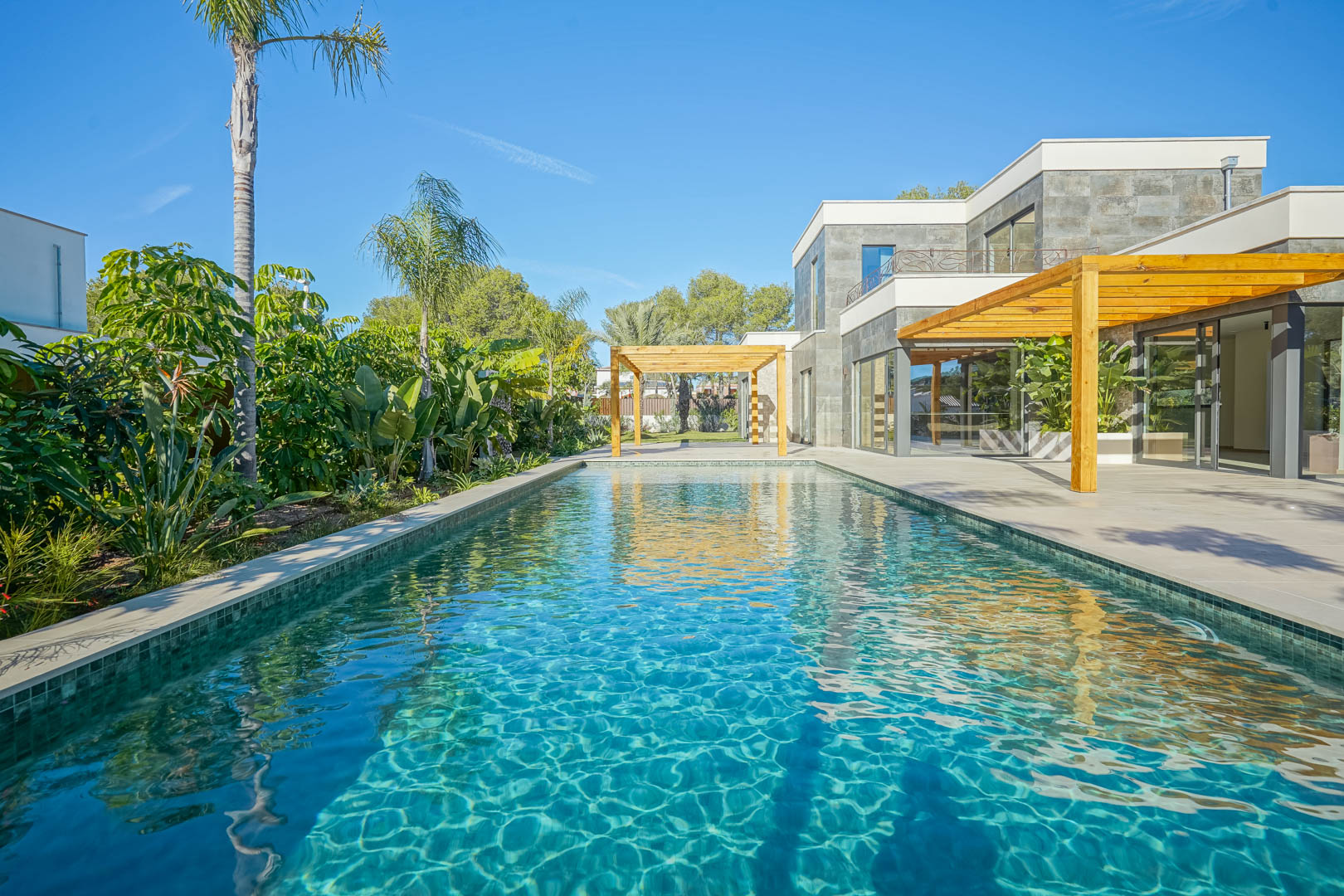 Piscine de style Bali aux tons émeraude, bordée d'une terrasse spacieuse avec pergolas en bois d'iroko et un jardin méditerranéen luxuriant.