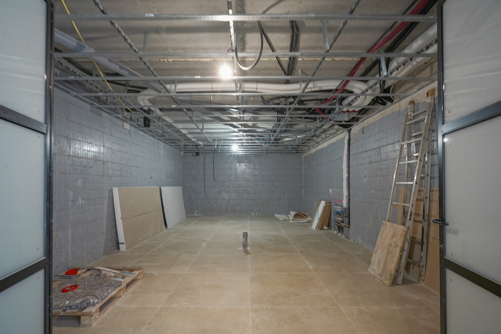 Sous-sol polyvalent de 180 m2 en cours de finition avec murs isolants Styro Stone, structure de plafond technique et grandes portes coulissantes.