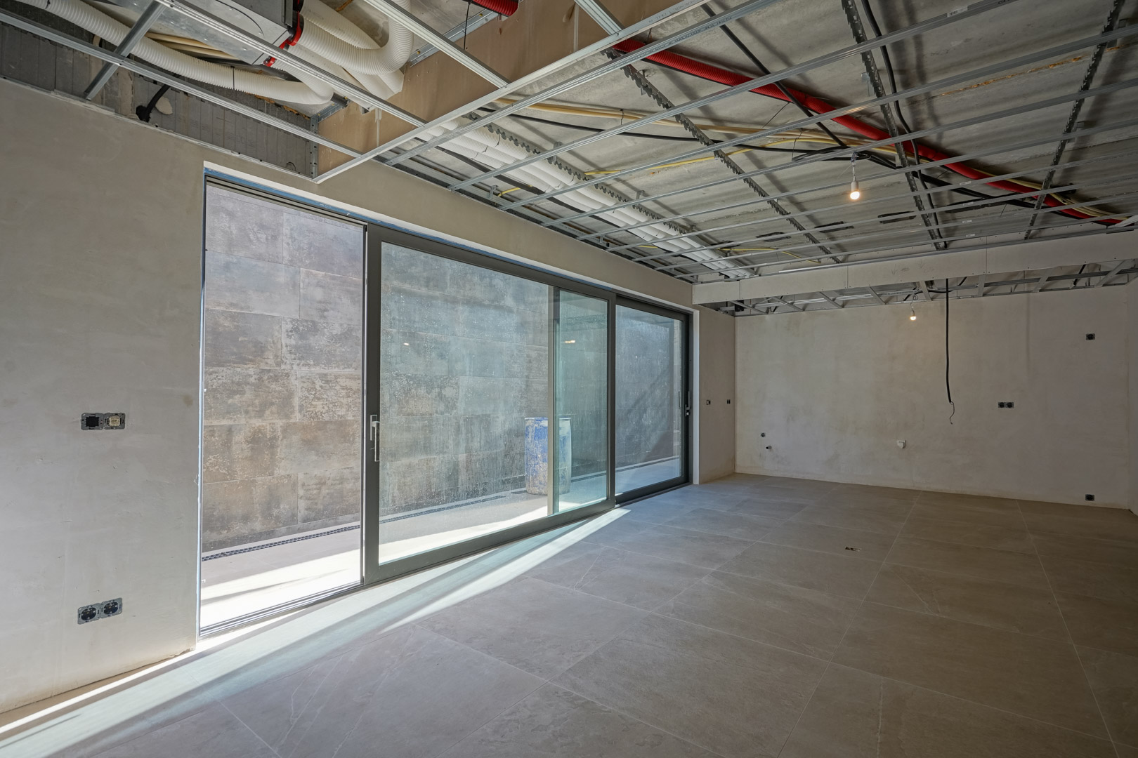Sous-sol spacieux en cours de finition avec de grandes baies vitrées coulissantes, un sol en grès cérame et des installations techniques apparentes au plafond.