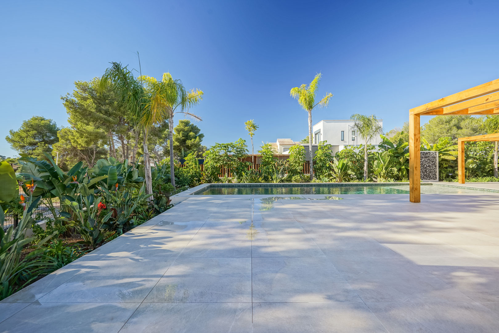 Terrasse en grès cérame bordant une piscine style Bali, agrémentée de pergolas en bois d'iroko et d'un jardin méditerranéen luxuriant.