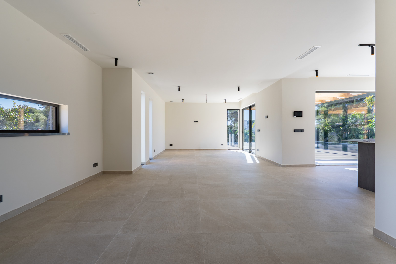 Vaste espace de vie ouvert avec carrelage grand format, éclairage minimaliste et baies vitrées coulissantes menant à la terrasse ensoleillée.