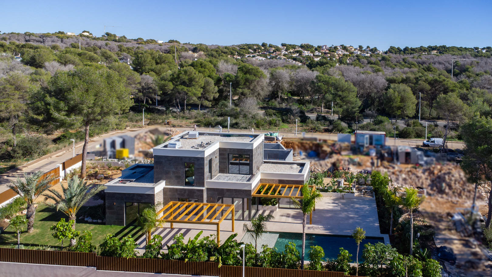 Vue aérienne de la villa moderne affichant une façade en pierre sombre, des pergolas en bois d'iroko et une piscine au cœur d'un jardin méditerranéen.